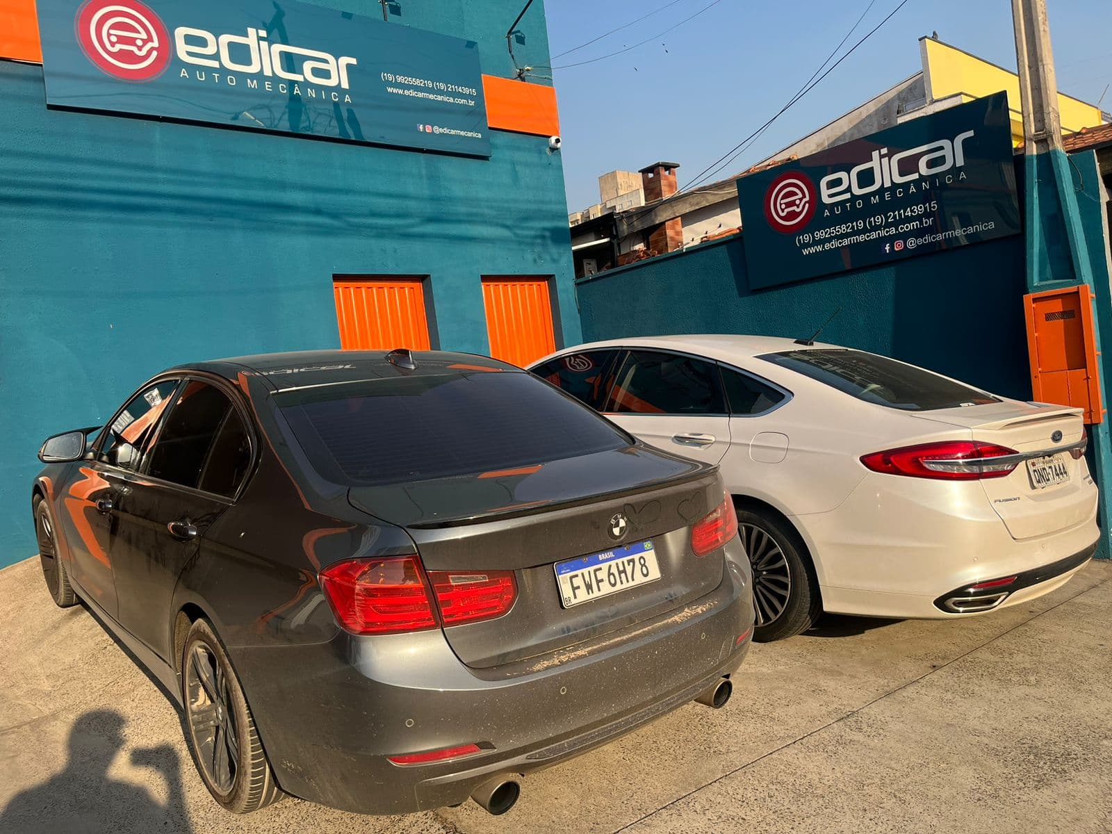 Fachada da Edicar: parede turquesa, portas laranja e a placa com o logo, com dois carros estacionados na frente
