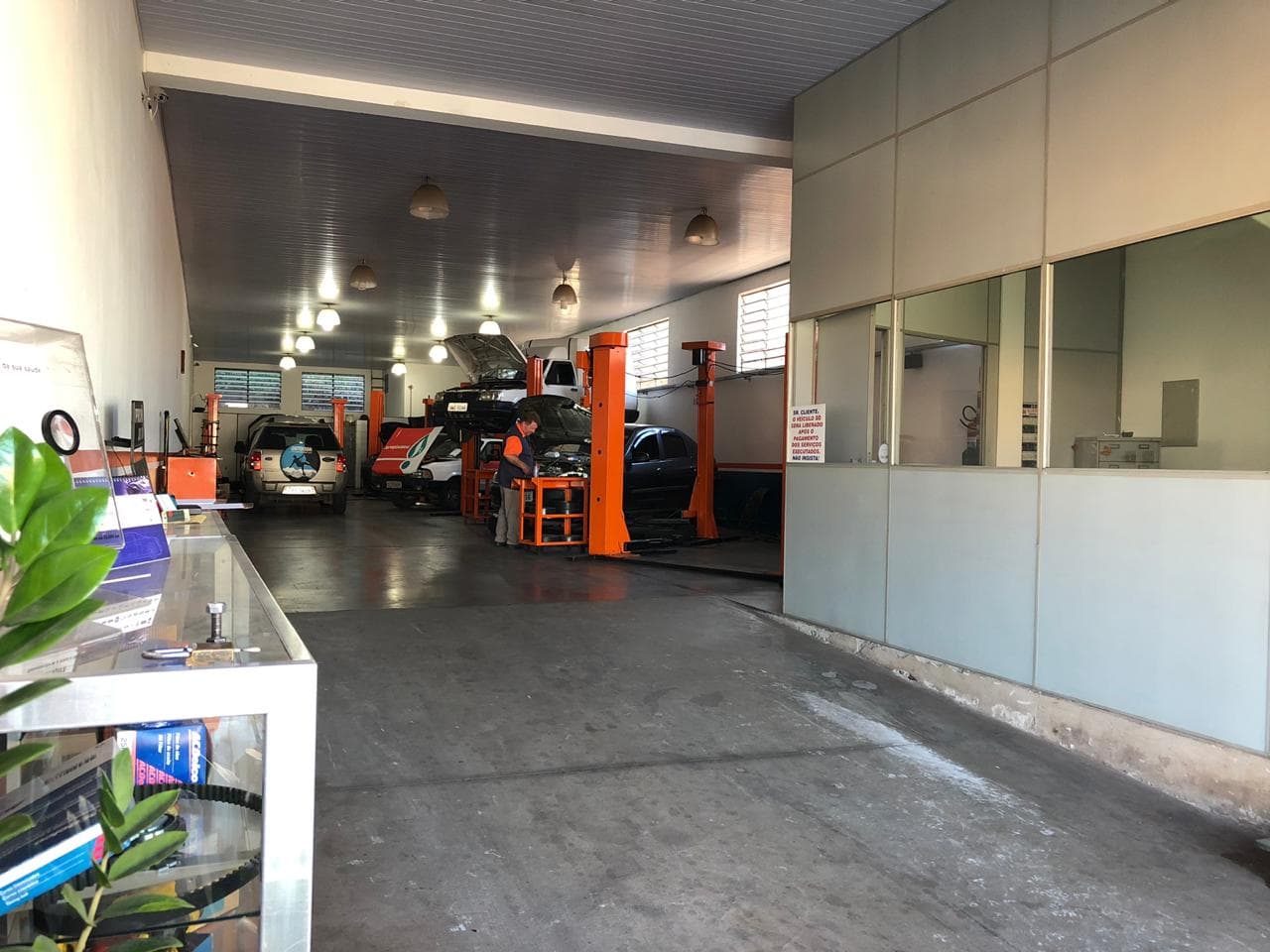 O salão da Edicar visto da entrada: piso limpo, carros nos elevadores laranja e a recepção de vidro à direita