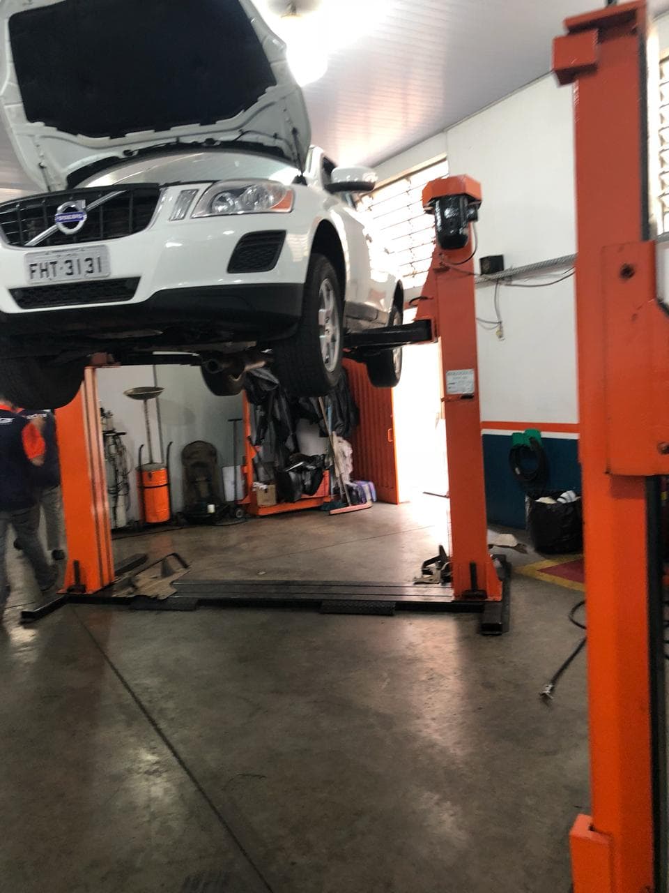 Volvo XC60 suspenso no elevador laranja, com o mecânico trabalhando embaixo